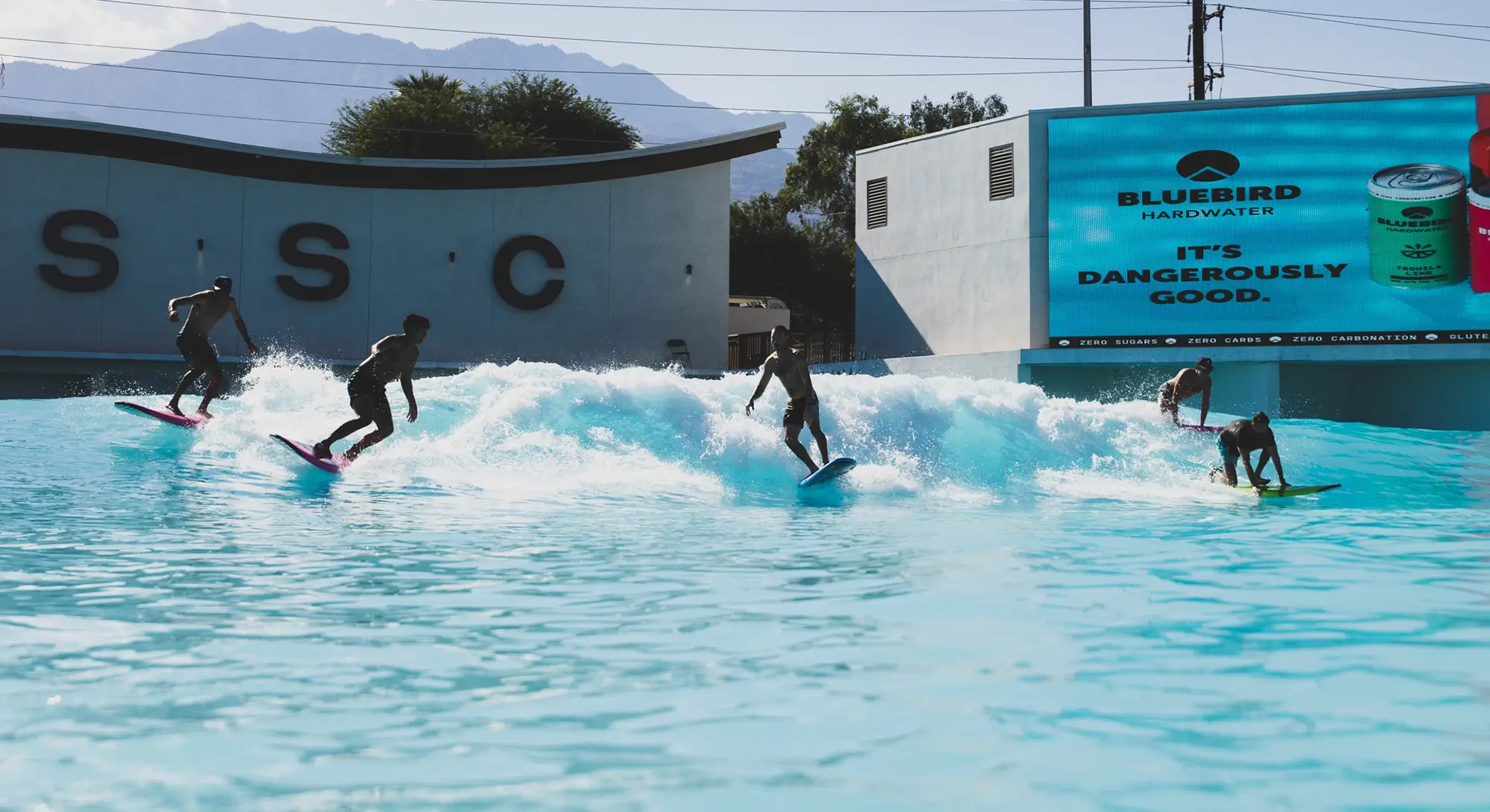 Group surf session at Palm Springs Surf Club wave pool with riders on the wave in the desert