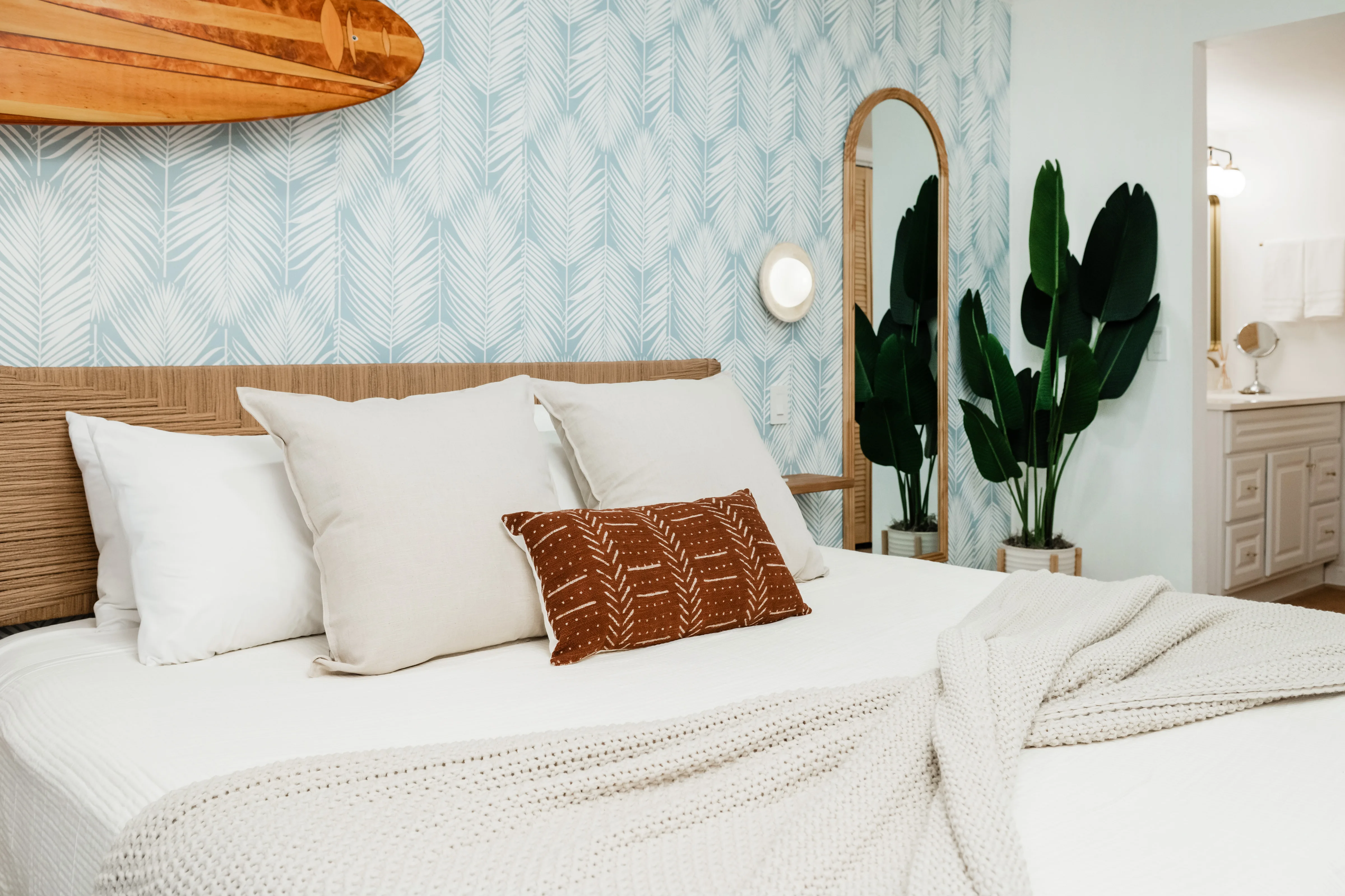 The Sundune Palm Springs bedroom with surfboard mounted above the bed, tropical palm leaf wallpaper, and rattan headboard