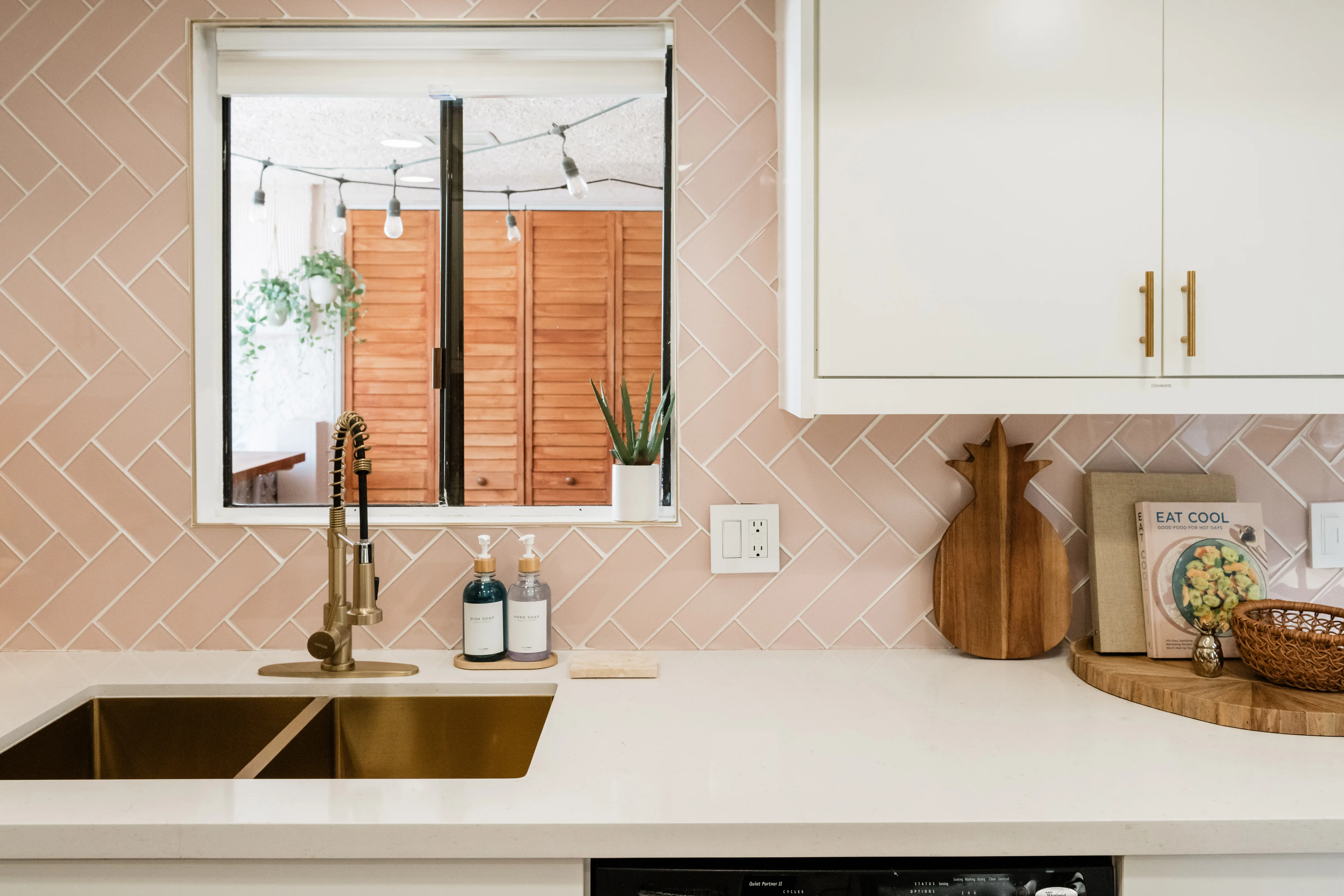 The Sundune Palm Springs kitchen with pink herringbone tile backsplash, gold faucet, white quartz countertops, and patio view through the window