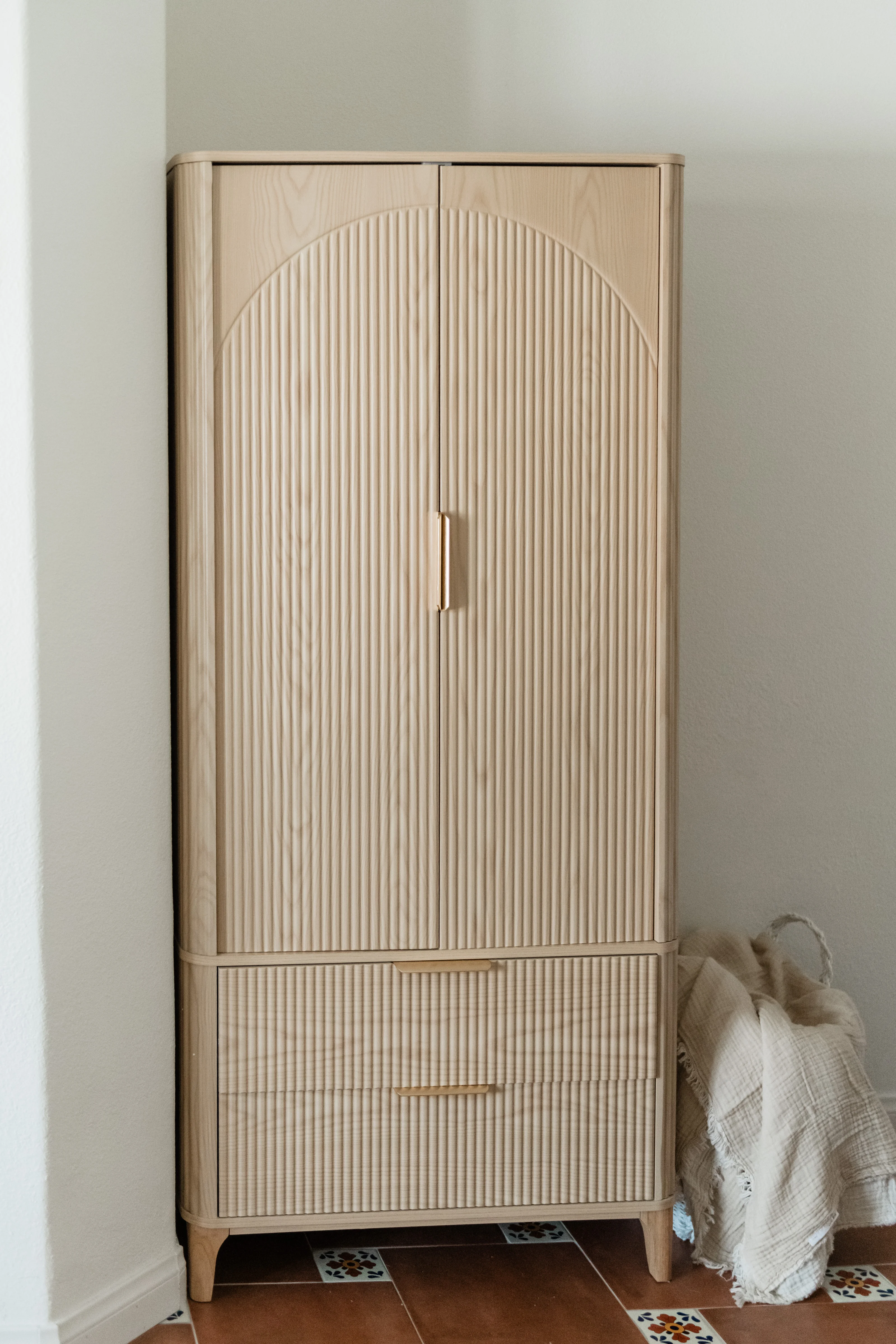 Natural wood ribbed armoire with arched doors and brass handles in the Cali Room at Terra Luz, with Talavera tile floor in Indio California