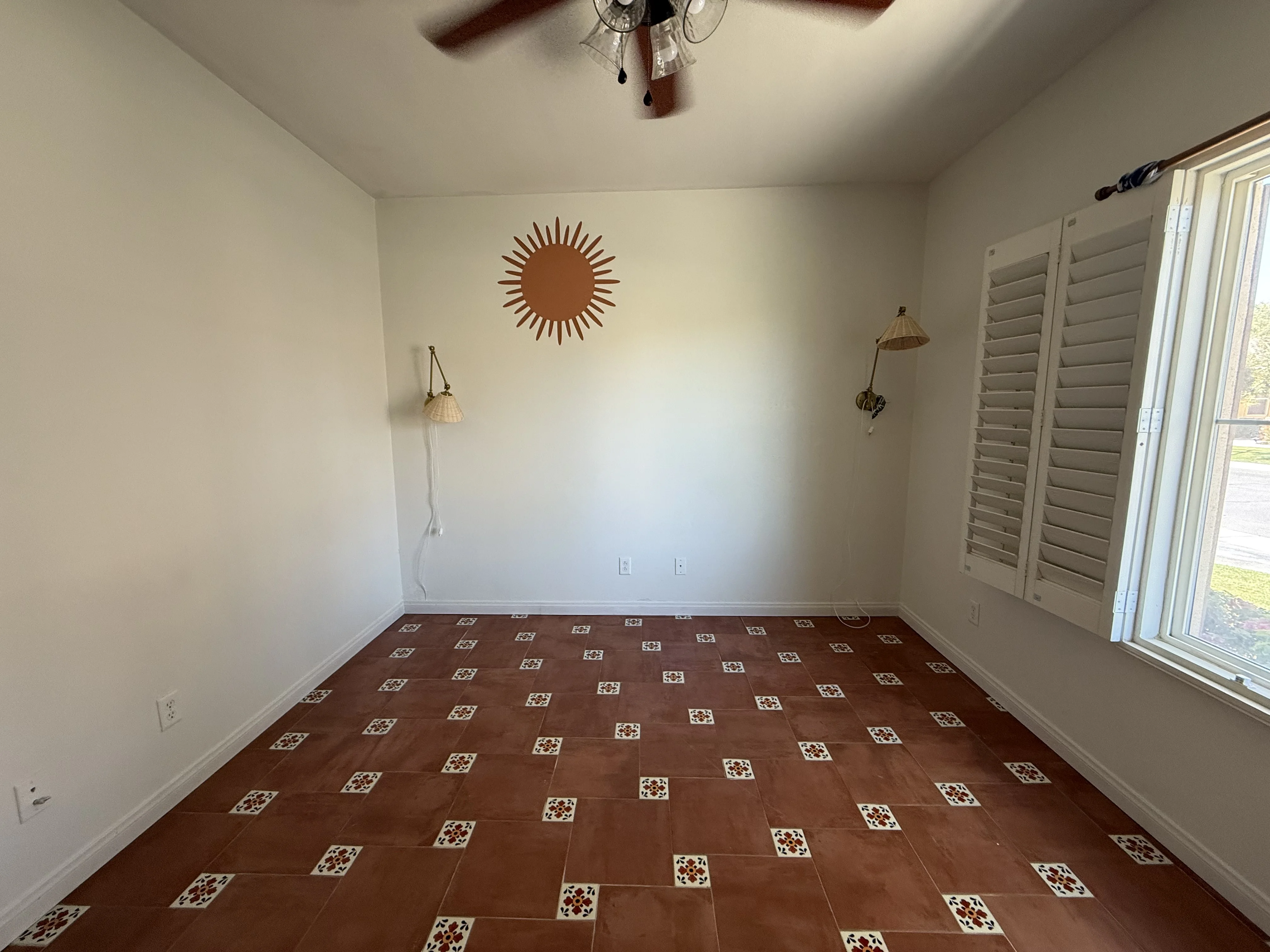 Cali Room at Terra Luz before the headboard was installed — bare white walls, terracotta Talavera tile floor, brass sconces, and sun wall art in Indio California