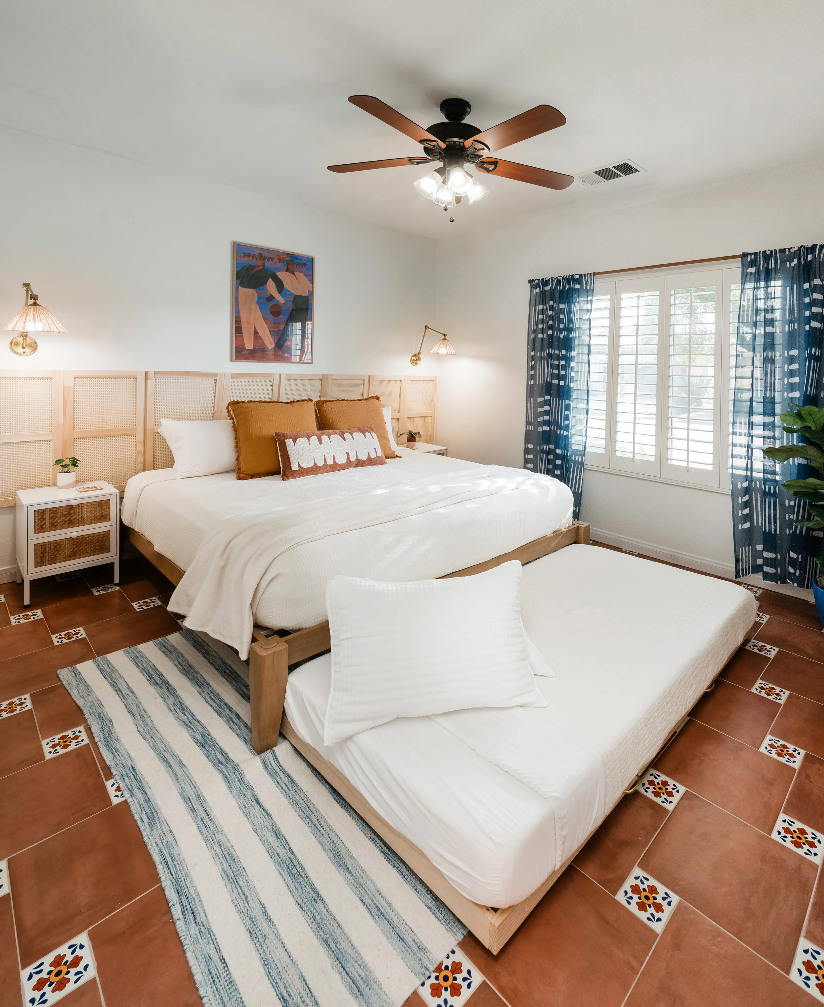 Cali Room at Terra Luz with king bed and trundle both extended, showing full wall-to-wall rattan cane panel headboard, amber pillows, and shibori curtains