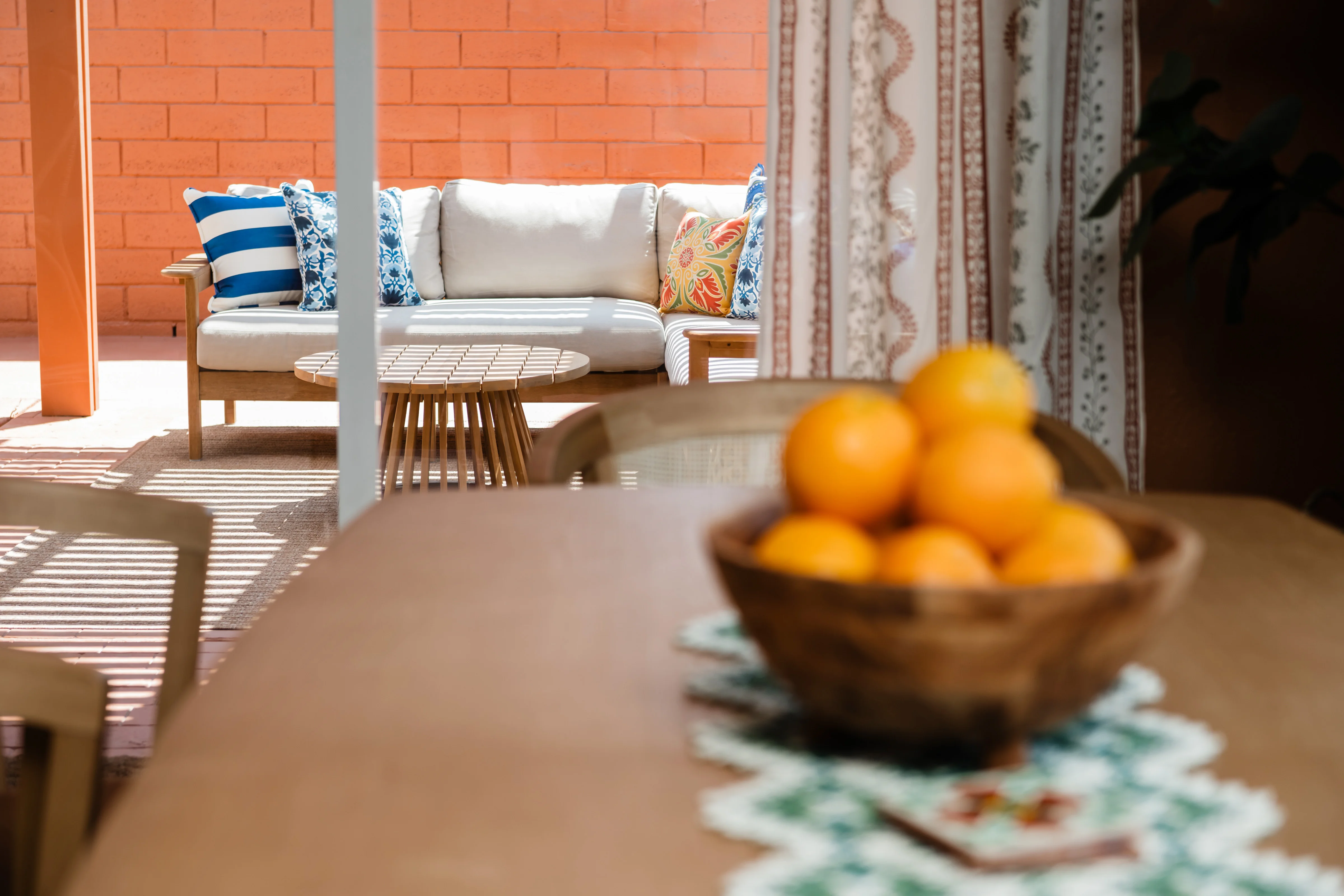 Terra Luz dining table with wooden bowl of oranges and Talavera tile coasters, glass doors open to the pool patio in Indio California