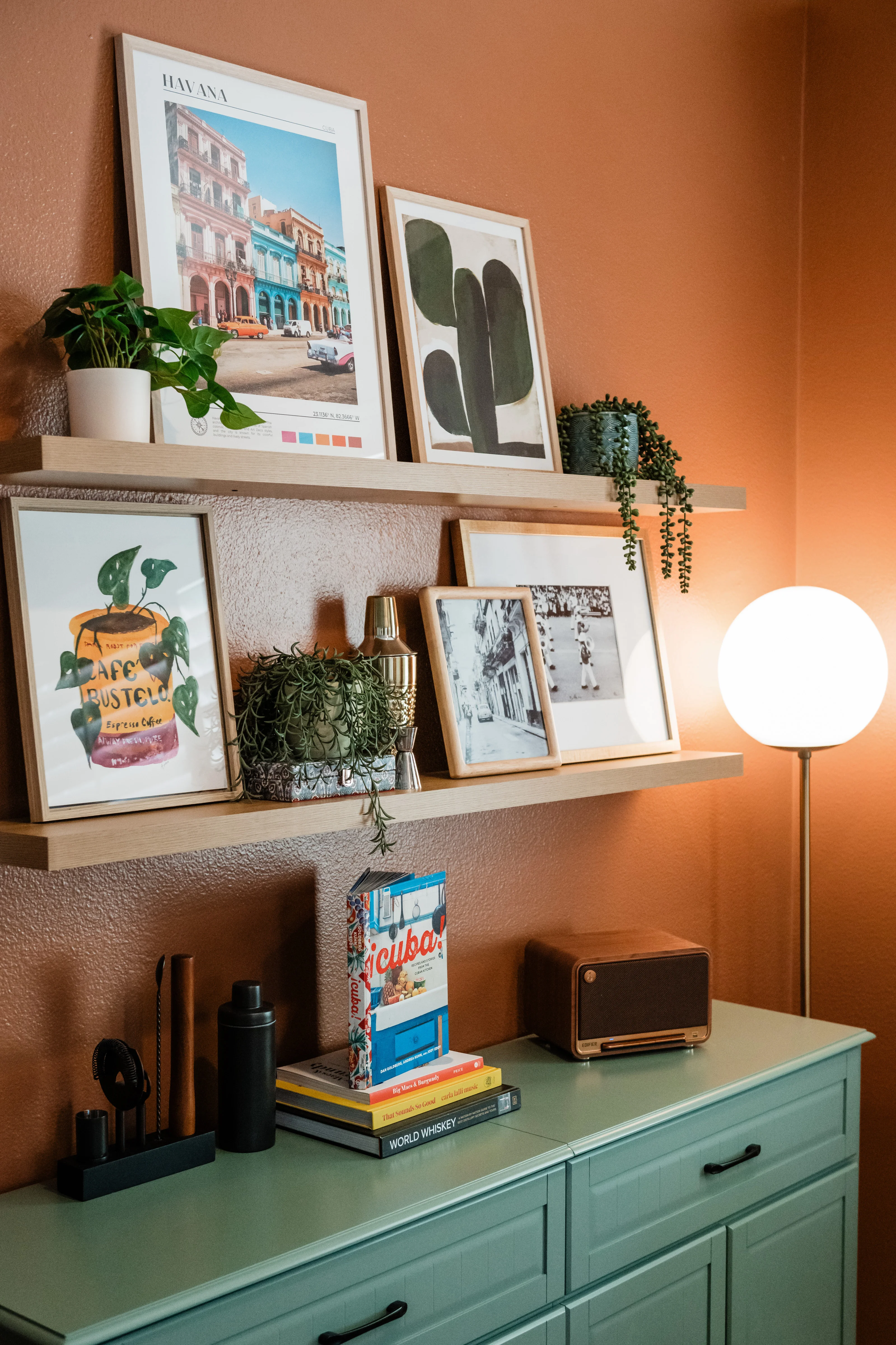 Teal credenza with Cuba travel books and retro radio, floating shelves with Havana street print, Cafe Bustelo art, and black and white photography against the terracotta wall at Terra Luz
