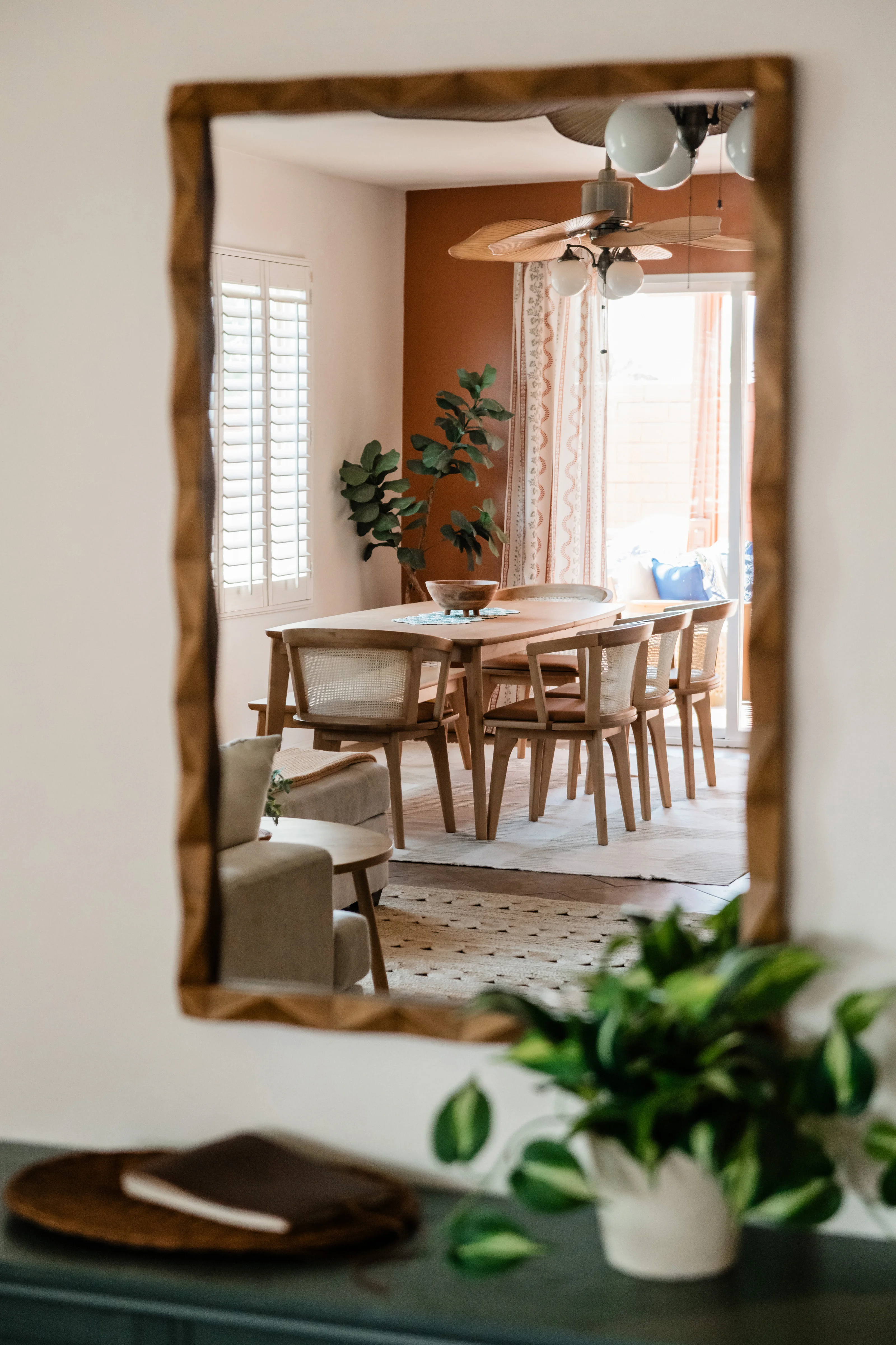 Terra Luz dining table set for eight with rattan bistro chairs, wooden fruit bowl with oranges, teal geometric table runner, and terracotta walls in Indio California