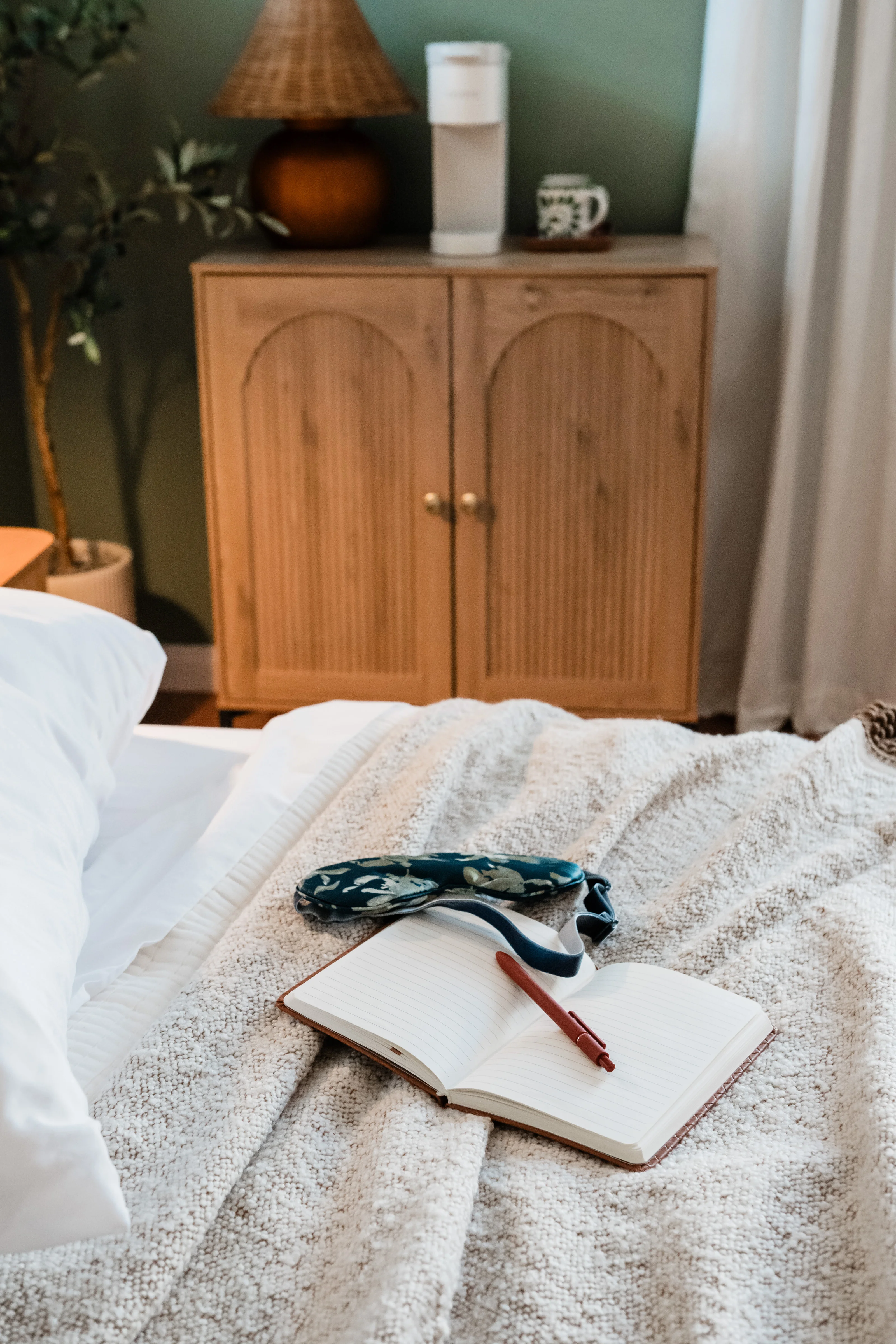 Primary bedroom at Terra Luz with sage green walls, arched wood cabinet coffee station, wicker lamp, and king bed with textured white bedding