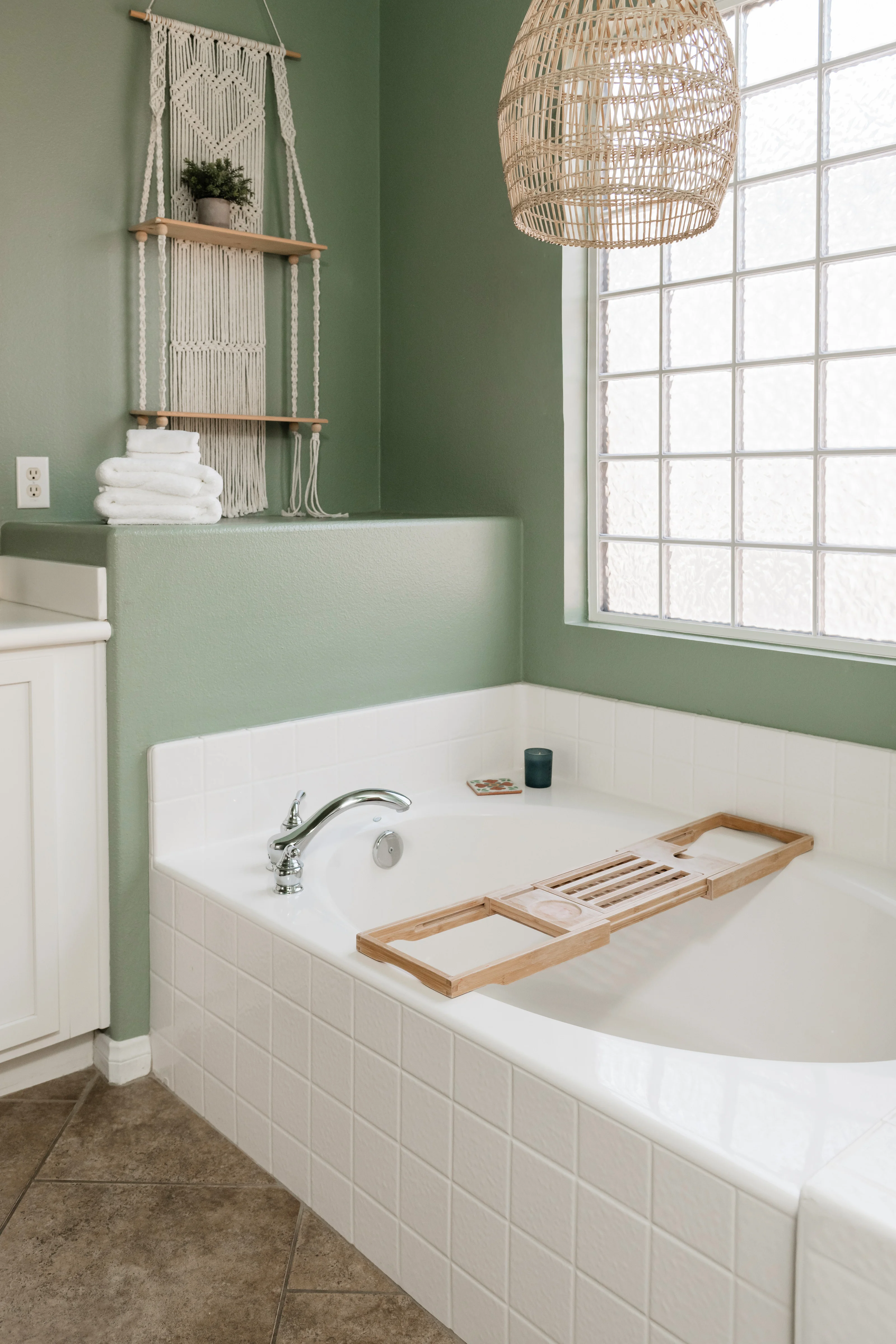 Primary ensuite bathroom at Terra Luz with sage green walls, soaking tub, macrame shelf, rattan pendant light, and wooden bath tray