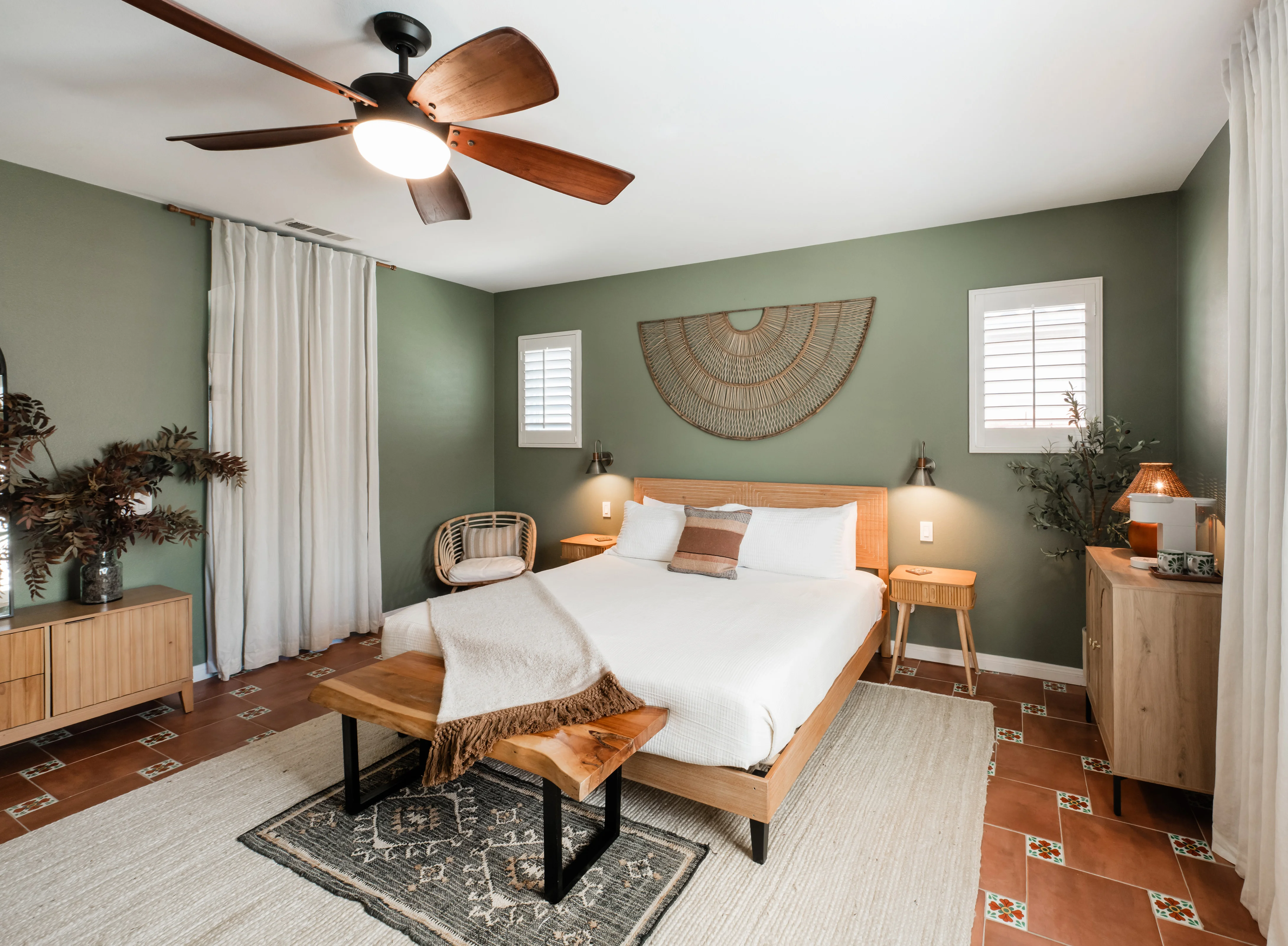 Terra Luz primary bedroom in Indio California with sage green walls, king bed with natural wood frame, rattan fan wall art, live-edge bench, and Talavera tile floor