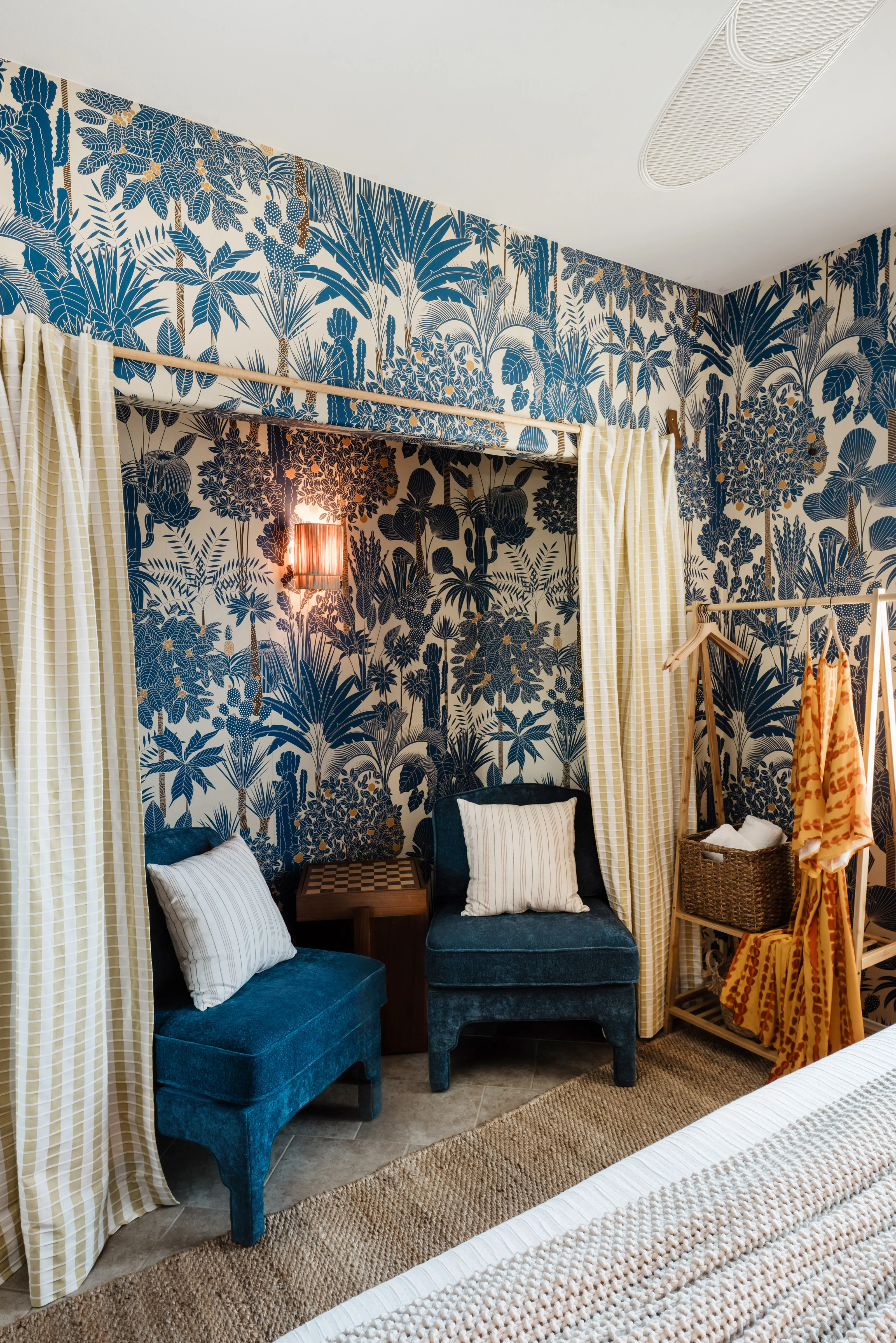 Seating nook in the Wild Tropics bedroom at Terra Luz, with gold and cream striped curtains framing wallpapered alcove and navy velvet chairs