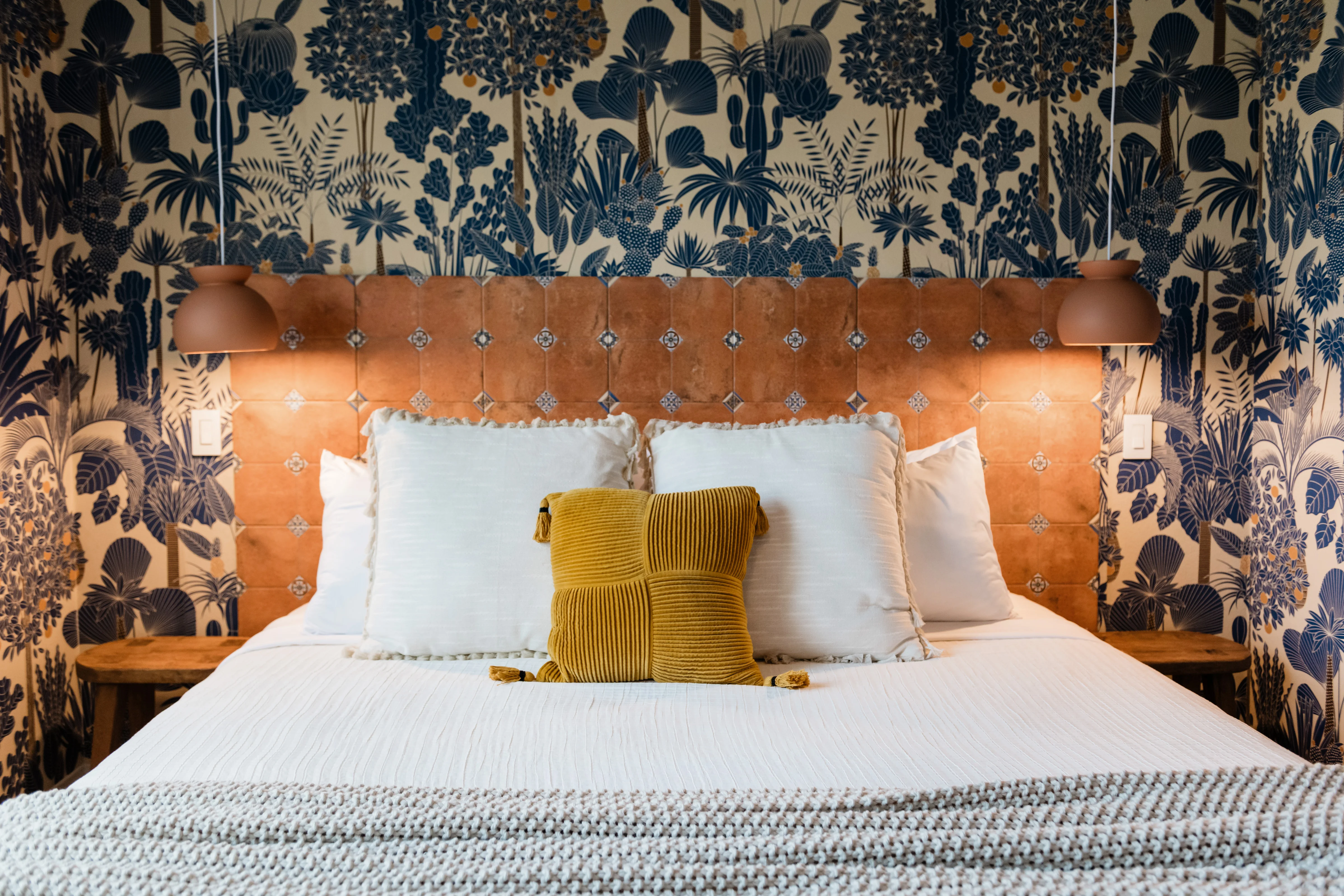 King bed with custom terracotta tile headboard and both pendant lamps glowing, Wild Tropics bedroom at Terra Luz vacation rental in Indio California