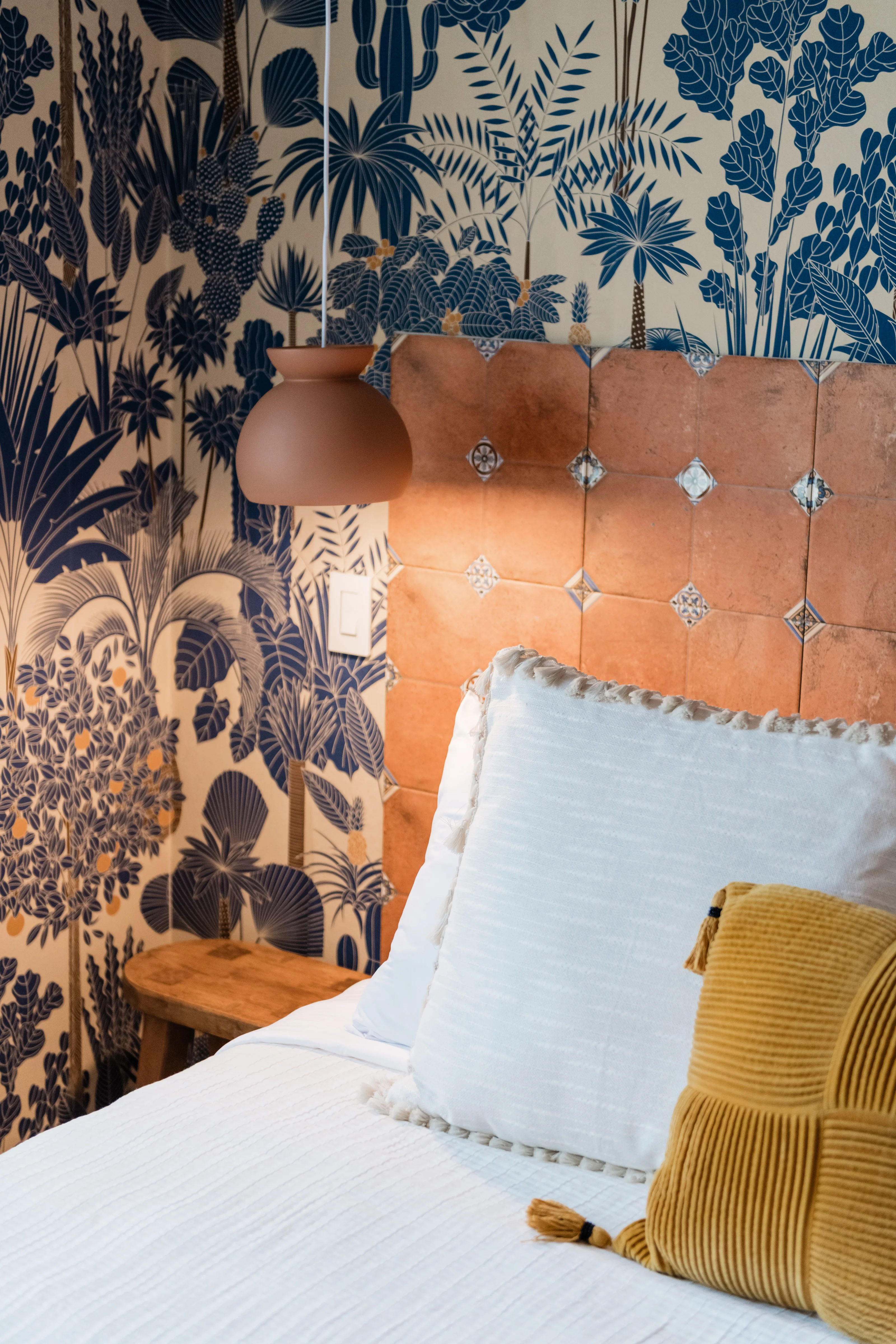 Terracotta pendant lamp and custom tile headboard detail in the Wild Tropics bedroom at Terra Luz, with Rebel Wall botanical wallpaper behind