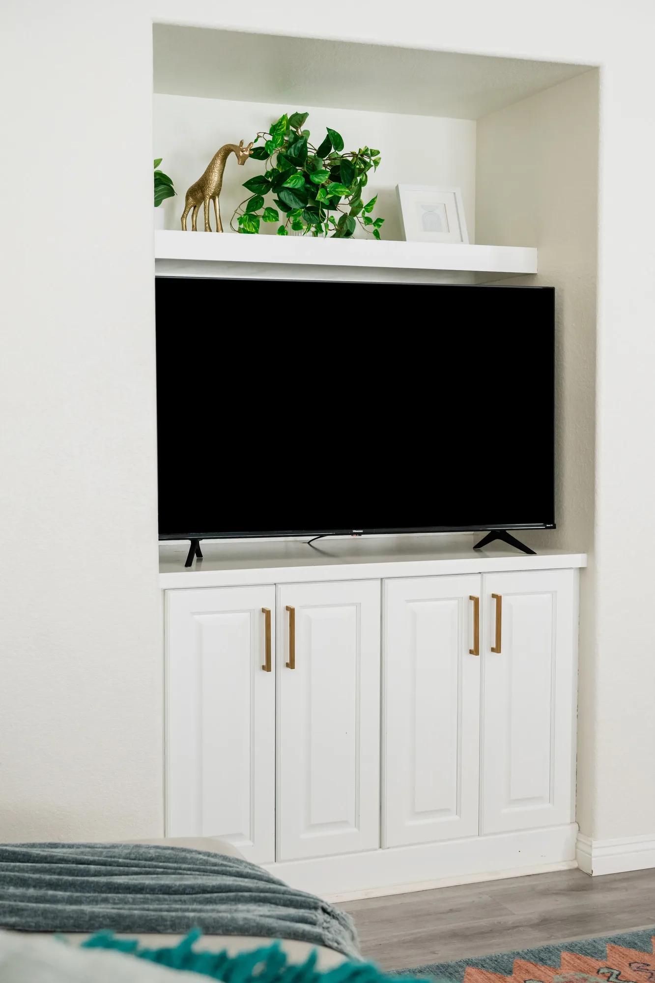 Cozy Cactus living room TV built-in niche with white cabinets, gold deer figurine, and trailing pothos