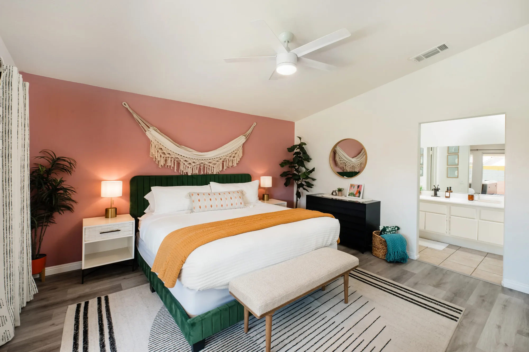 Cozy Cactus primary bedroom with pink accent wall, green velvet king headboard, and macrame art