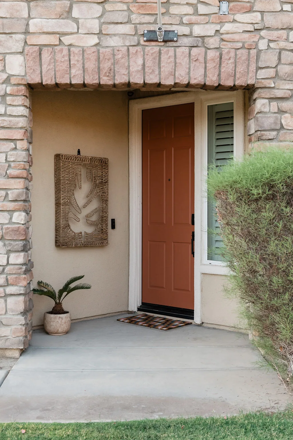 Terra Luz terracotta front door with stone arch and woven wall art