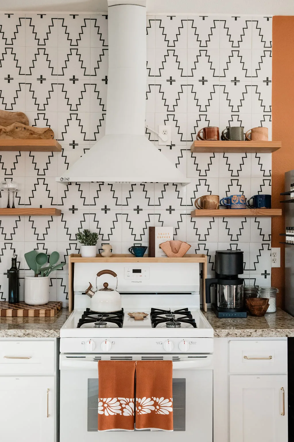 Terra Luz kitchen with geometric tile backsplash, floating wood shelves, and white gas stove