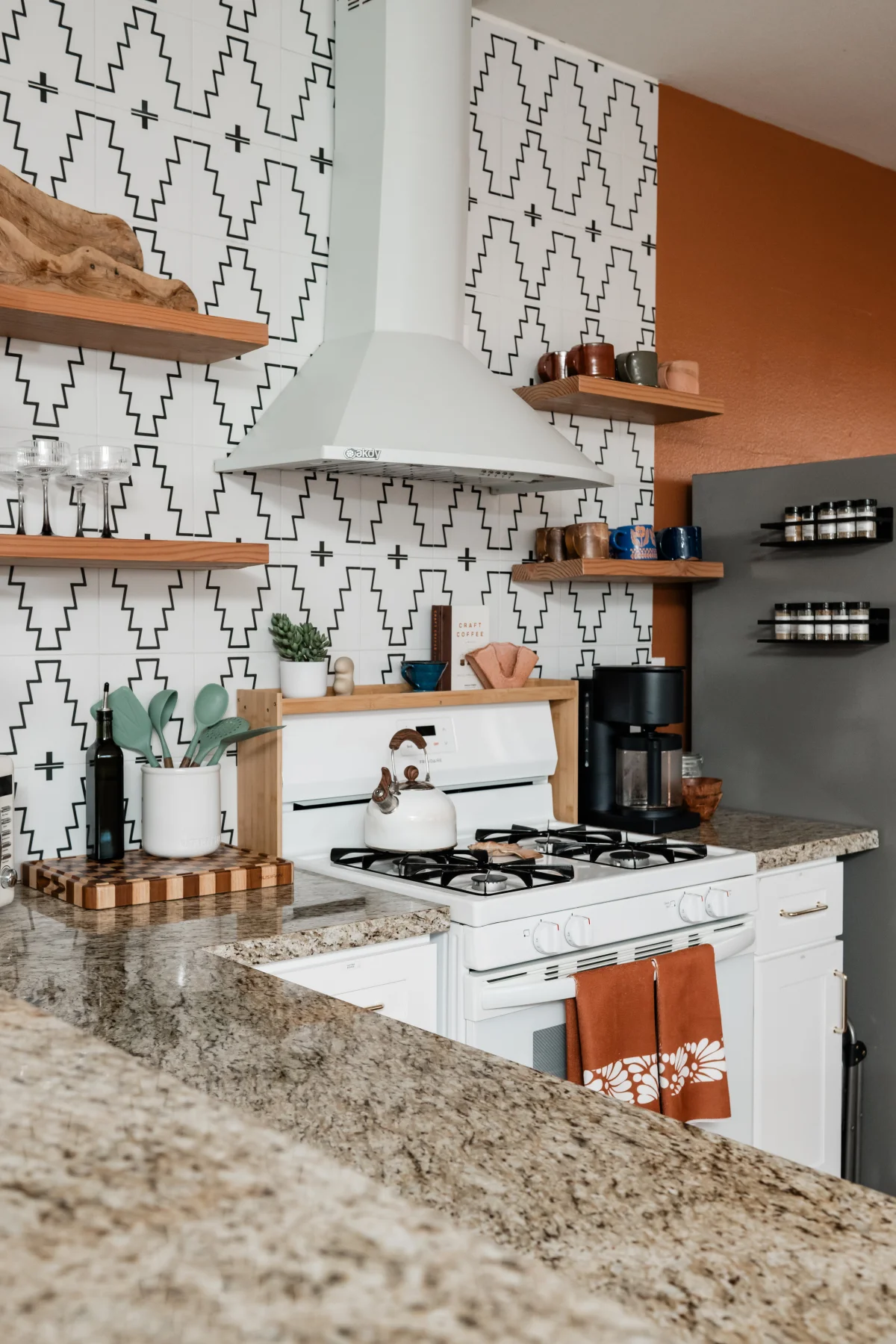 Terra Luz kitchen full view showing white gas stove, range hood, floating shelves, terracotta accent wall, and fridge