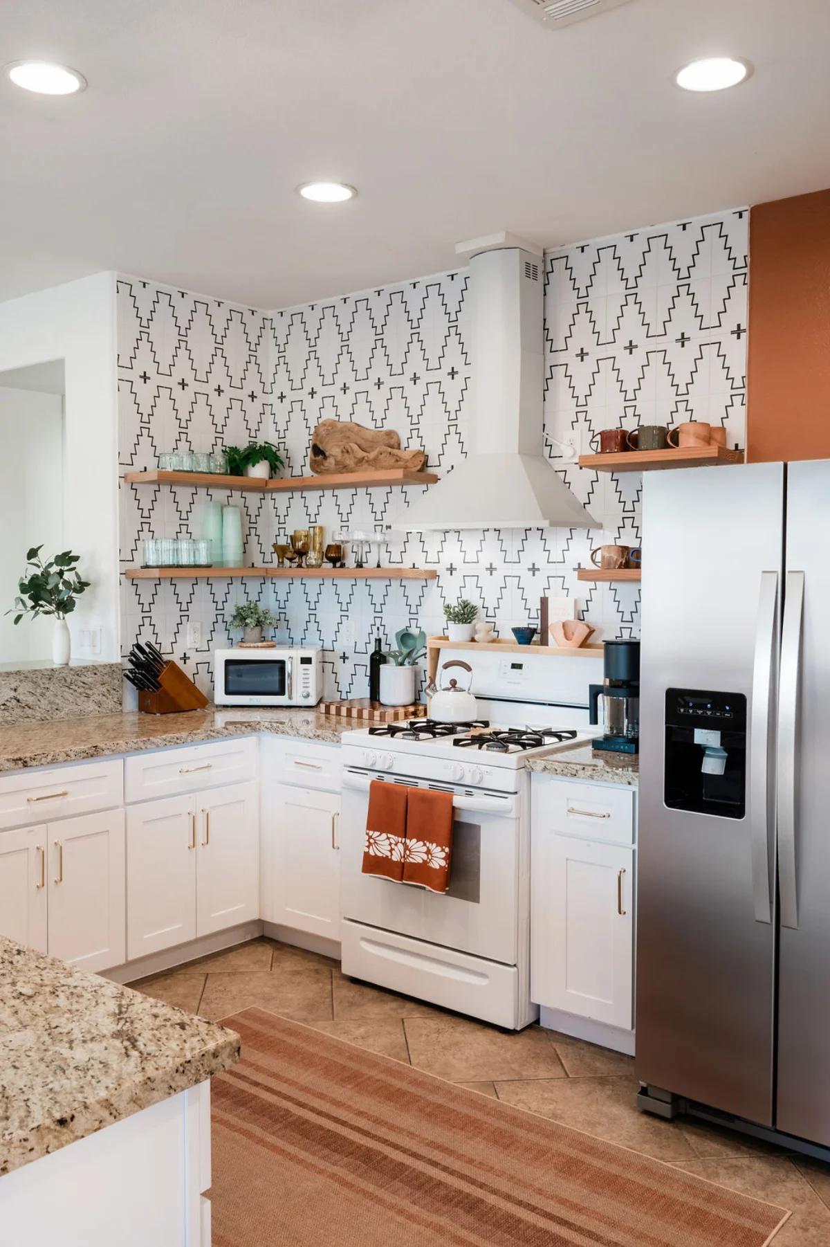 Terra Luz kitchen corner with gas stove, range hood, open wood shelves, and spice rack against geometric backsplash