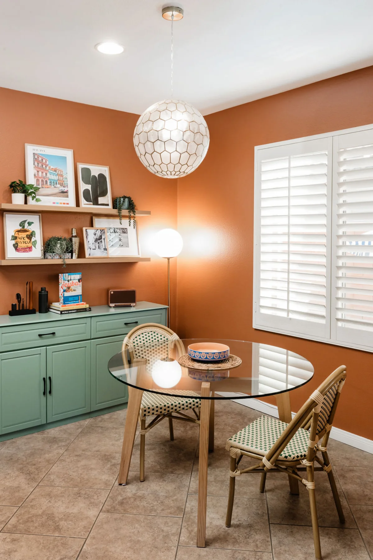 Terra Luz breakfast nook with glass round table, bistro chairs, capiz pendant light, and green credenza on terracotta walls