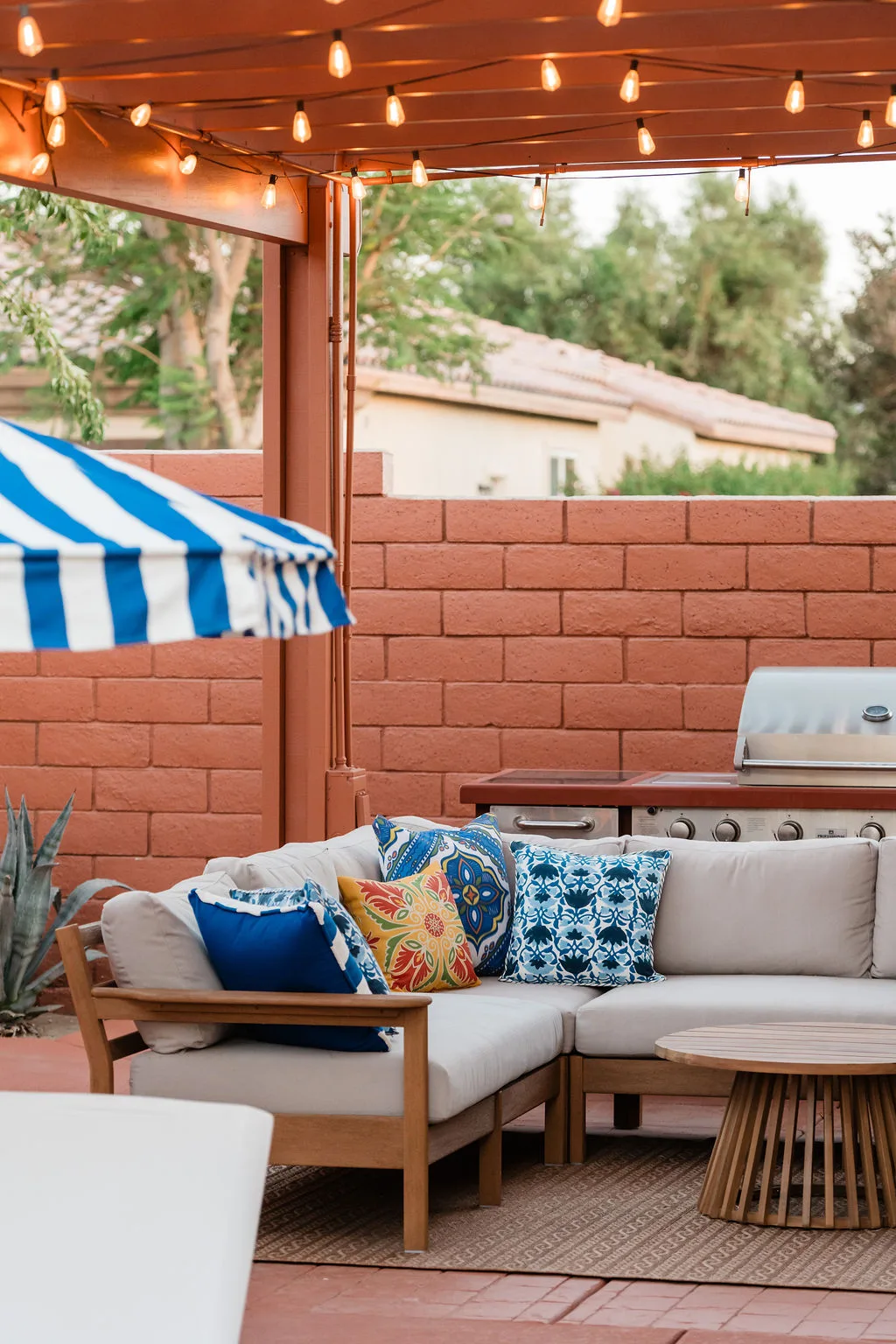 Terra Luz covered patio at dusk with string lights, outdoor sectional with colorful pillows, and grill
