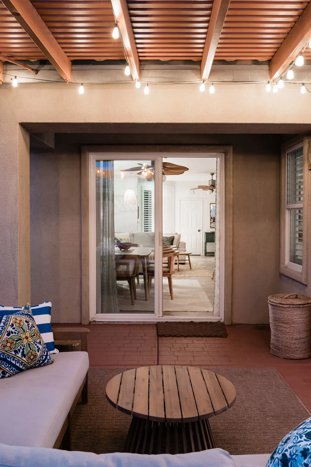Terra Luz covered patio at night with string lights looking through sliding glass door to lit dining room interior