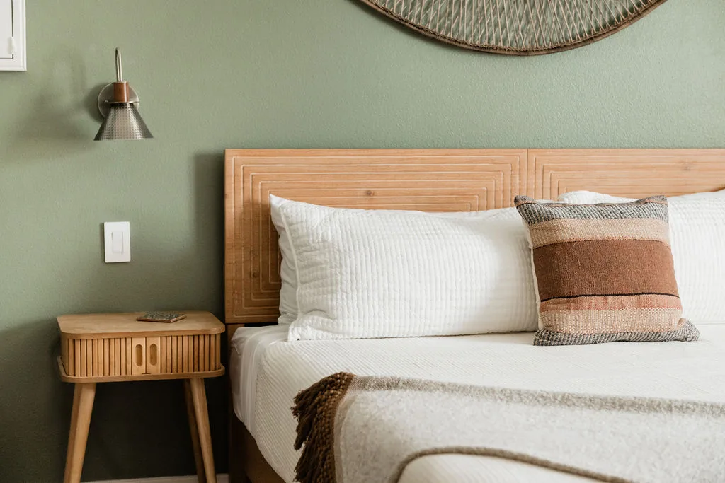 Terra Luz primary bedroom ribbed wood headboard with sage green walls, rattan wall sconce, and rattan circle mirror