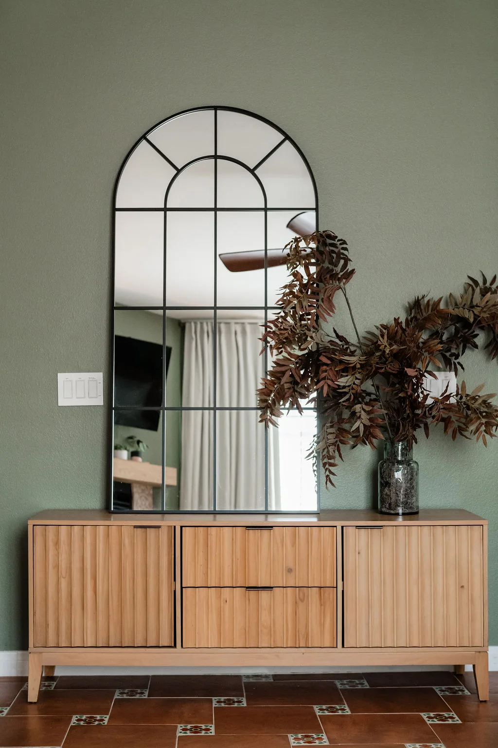 Terra Luz primary bedroom with arched mirror, ribbed wood credenza, and dried botanicals on custom tile floor