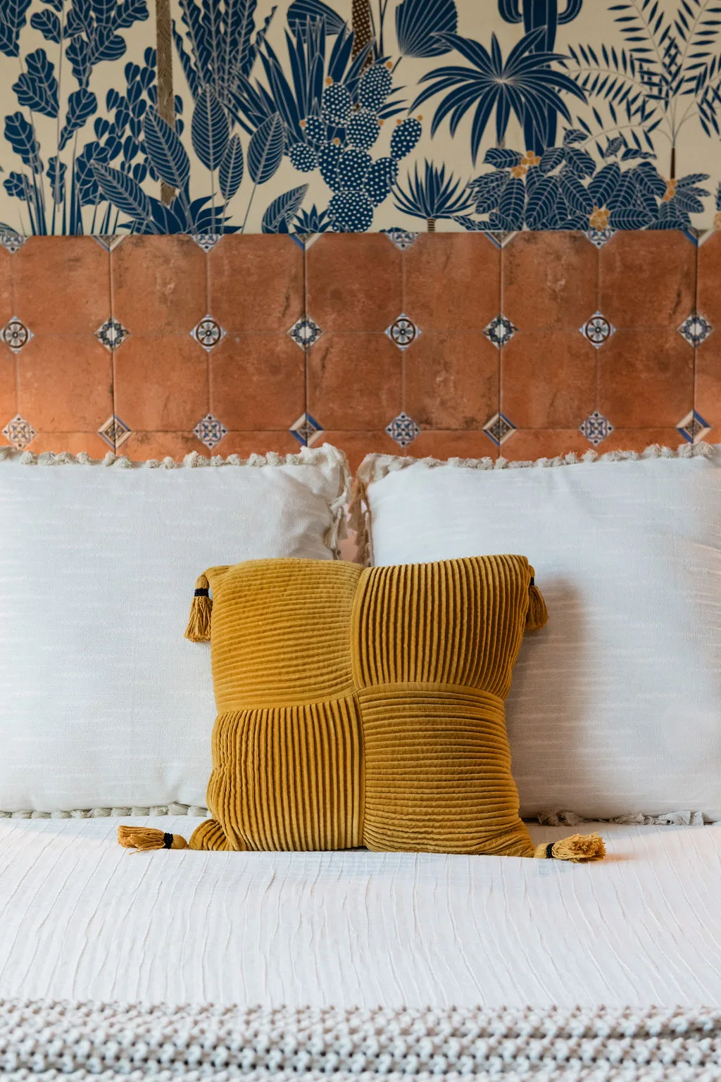 Terra Luz wallpaper bedroom custom cement tile headboard close-up with yellow decorative pillow and Rebel Wall tropical wallpaper