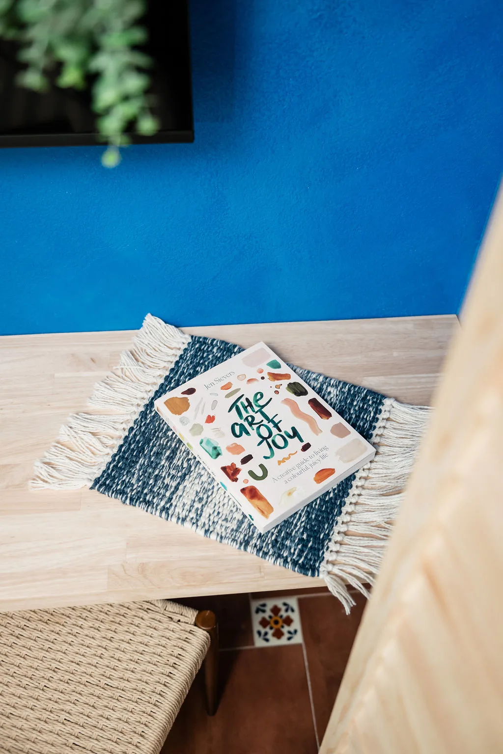 Terra Luz Cali bedroom floating wood desk with book on woven placemat against Kahlo blue accent wall
