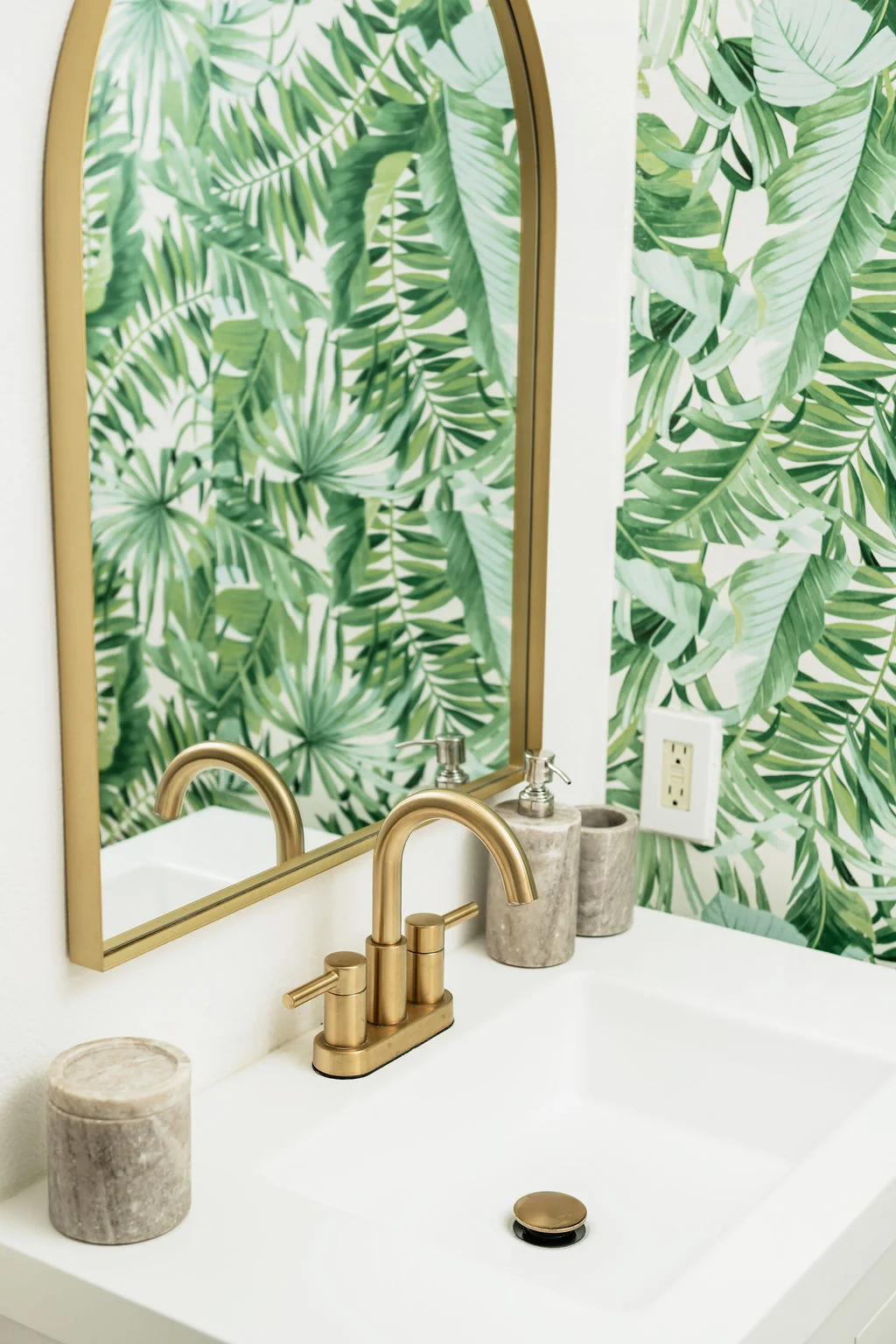 The Sundune Palm Springs primary bathroom with tropical palm leaf wallpaper, arched gold mirror, and gold faucet