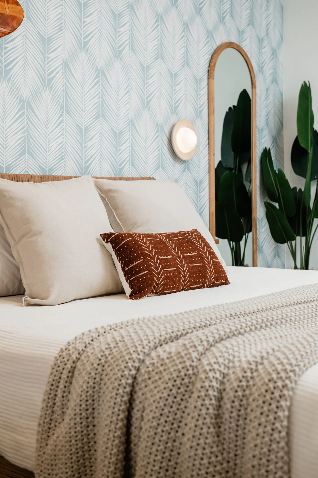 The Sundune Palm Springs primary bedroom king bed with palm frond wallpaper and rust accent pillow